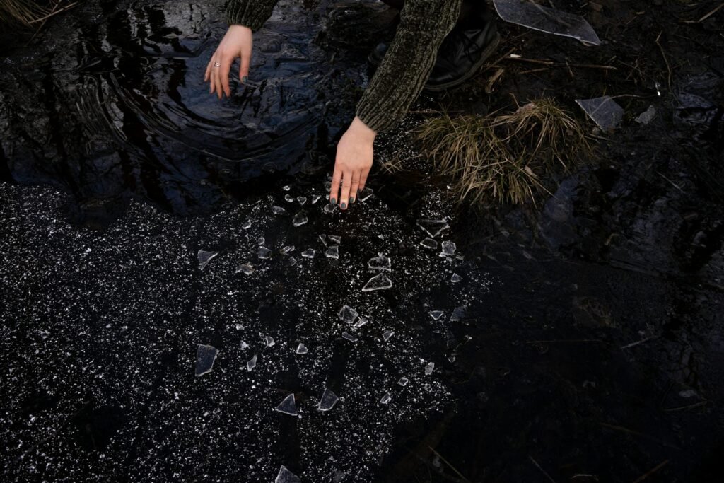 crop woman picking up broken glass near lake in countryside