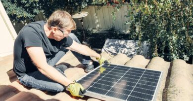 a man in black shirt sitting on the roof while holding a solar panel