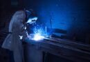 man wearing welding helmet welding metal near gray brick wall