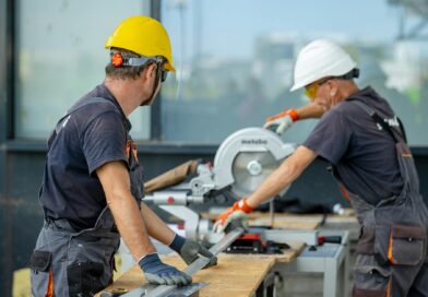 two workers cutting a metal beam with a saw