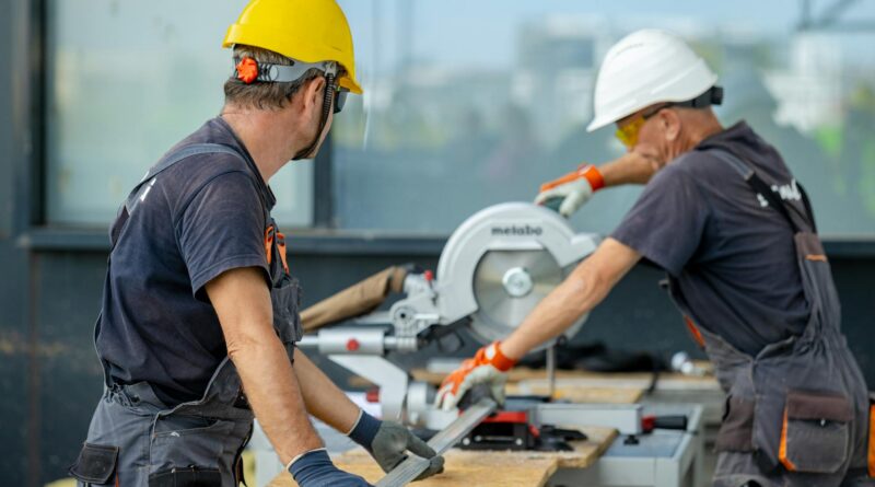 two workers cutting a metal beam with a saw