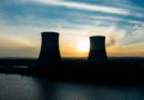 similar cooling towers near lake under bright sky at sunset
