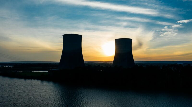 similar cooling towers near lake under bright sky at sunset